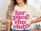 Cream t-shirt with pink "her pace run club" text in a retro font.