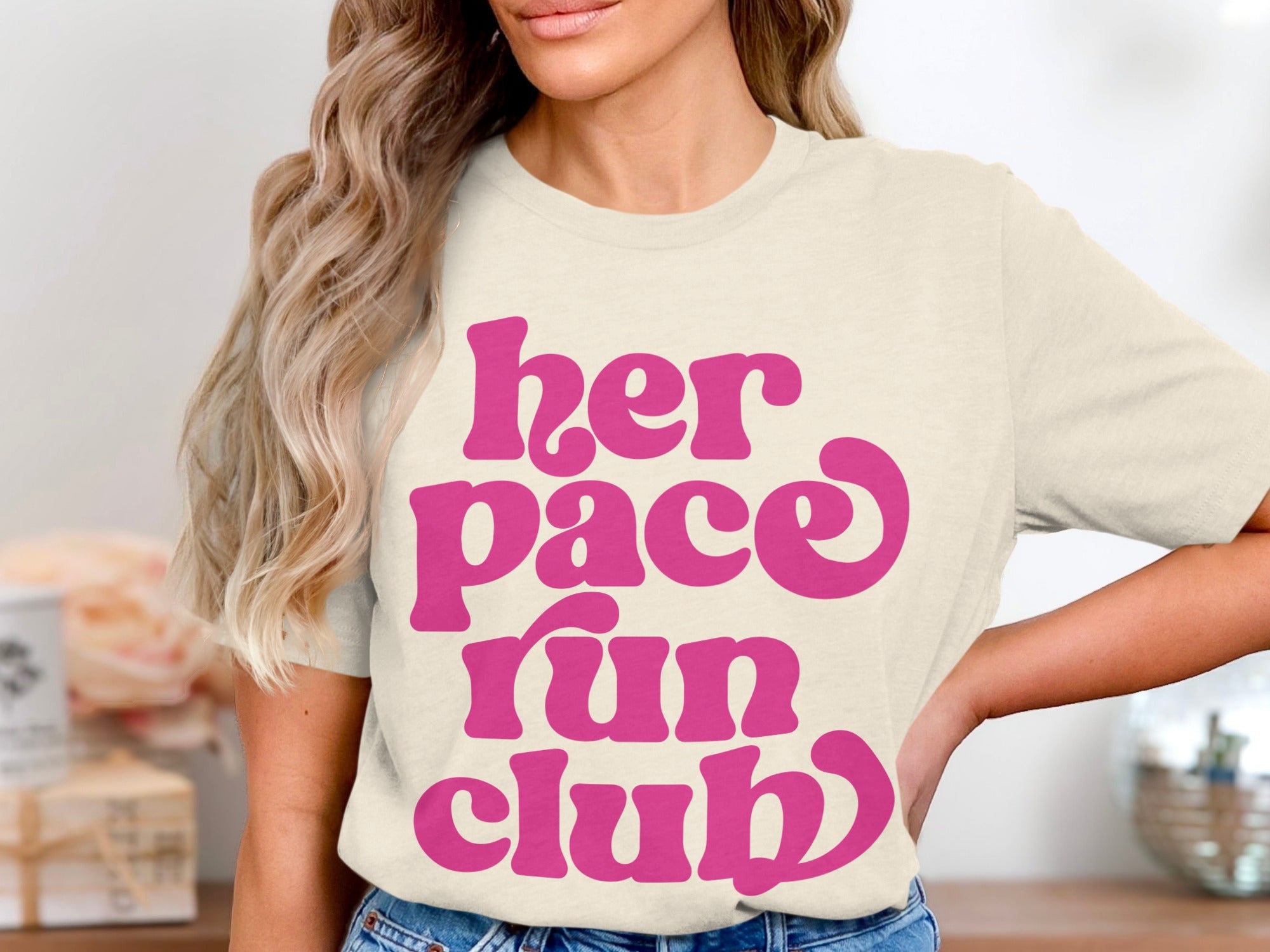 Cream t-shirt with pink "her pace run club" text in a retro font.