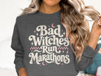 Dark gray sweatshirt with "Bad Witches Run Marathons" text and pink accents.
