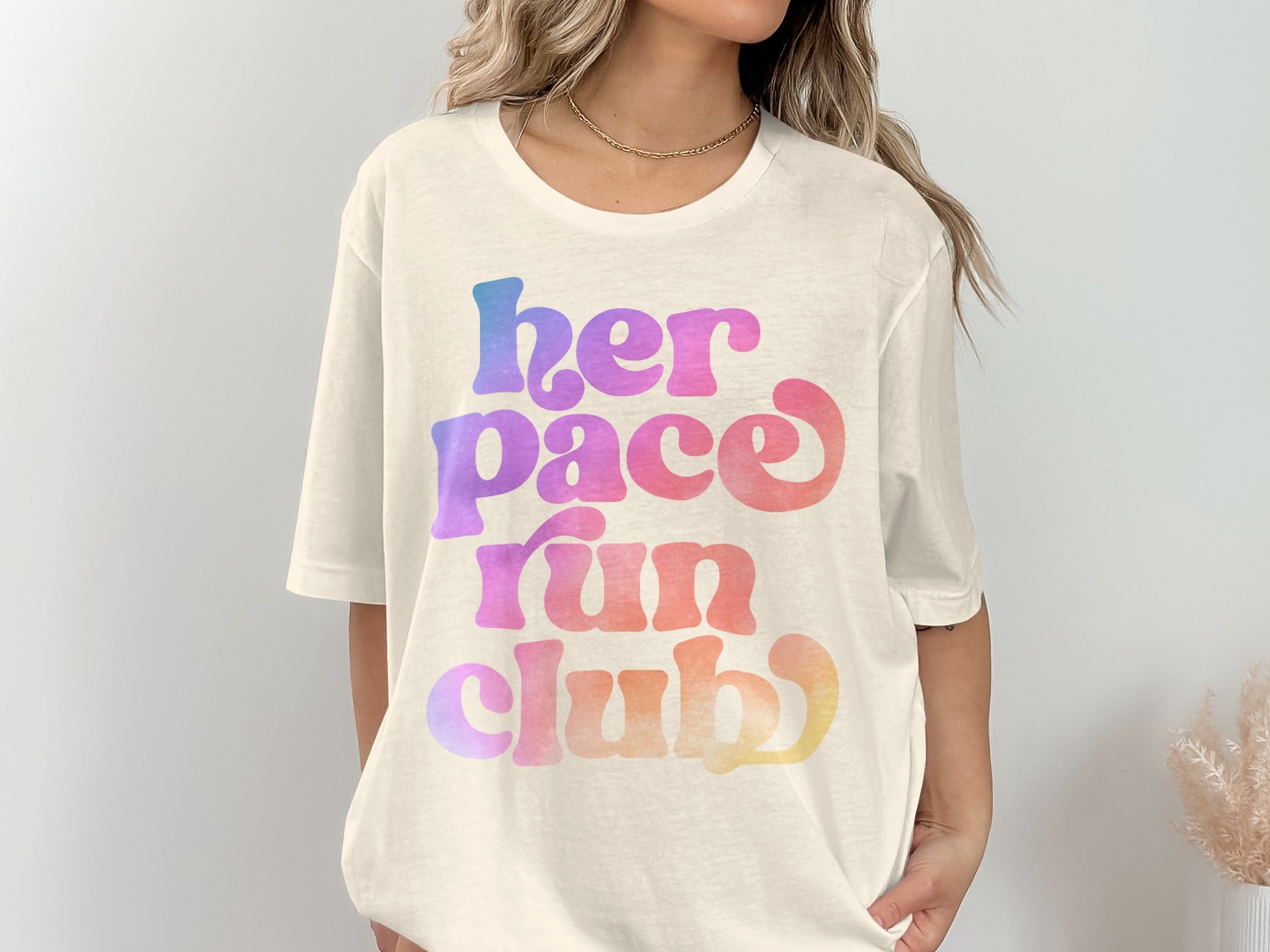 Cream t-shirt with rainbow gradient text reading "her pace run club".