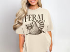 Cream t-shirt with "FERAL" text above a raccoon wearing sunglasses.