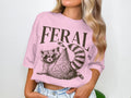 Pink t-shirt with "FERAL" text and a raccoon wearing sunglasses.