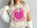 Cream t-shirt with pink "Long Miles Run High Vibes" graphic and a shoelace design.