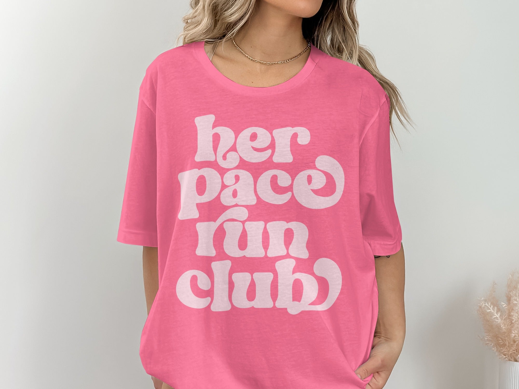 Pink t-shirt with white text "her pace run club" on the front.