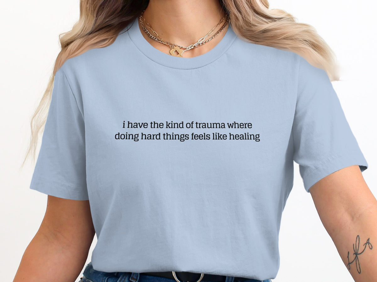 Light blue t-shirt with black text: "i have the kind of trauma where doing hard things feels like healing"