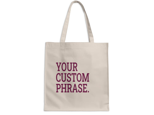 Beige tote bag with "YOUR CUSTOM PHRASE." text in maroon.