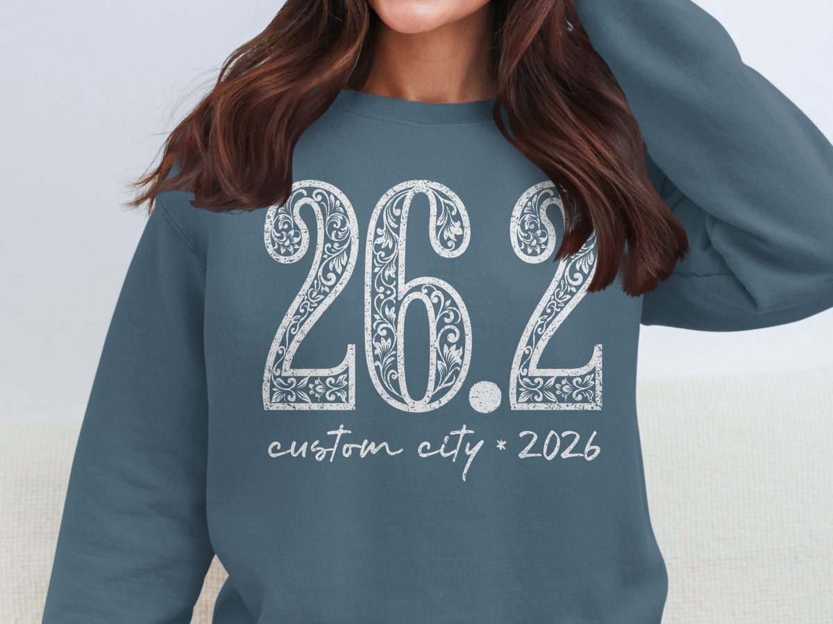 Blue sweatshirt with "26.2 custom city 2026" in white ornate lettering.