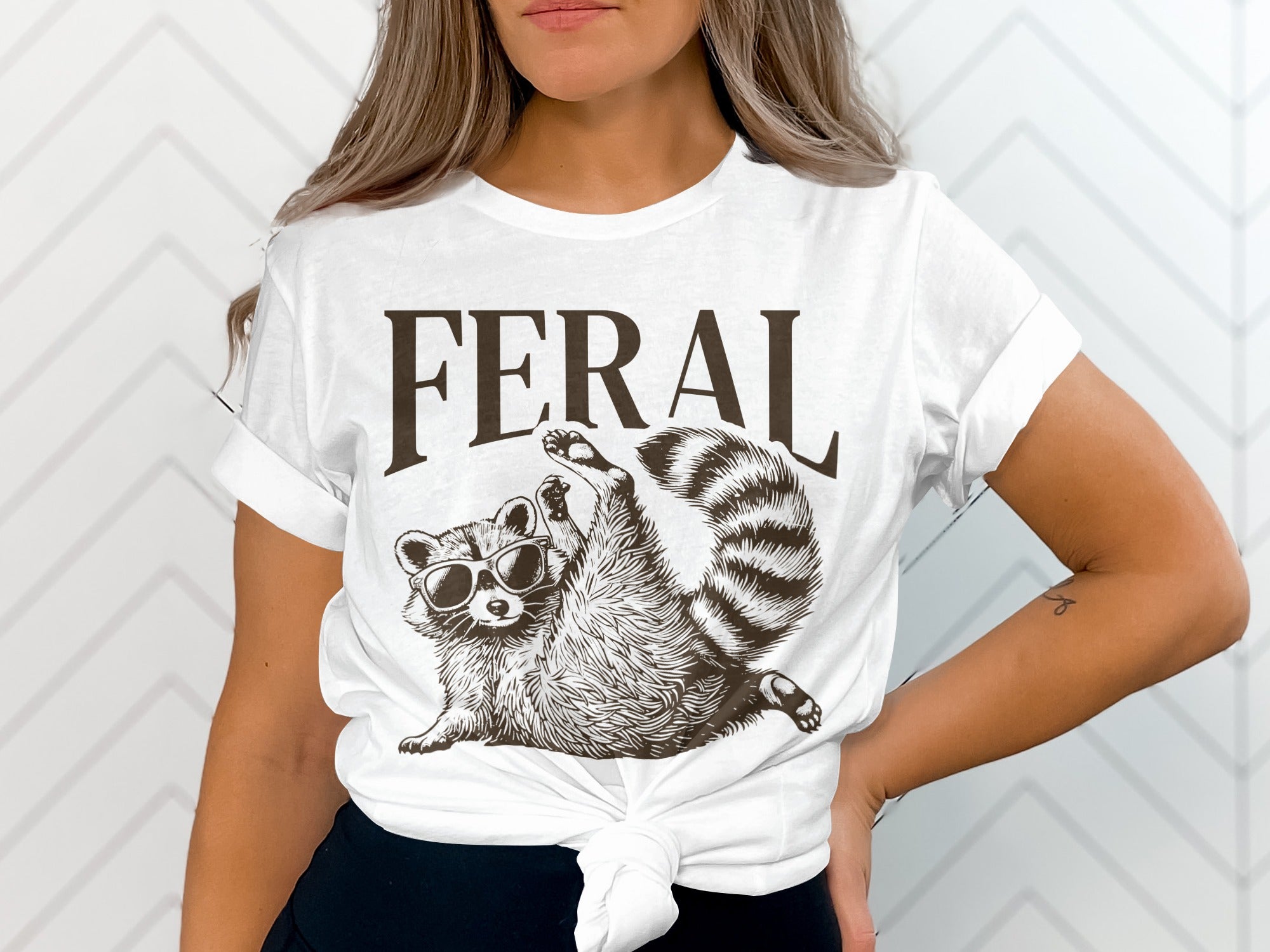 White t-shirt with "FERAL" and a raccoon wearing sunglasses.