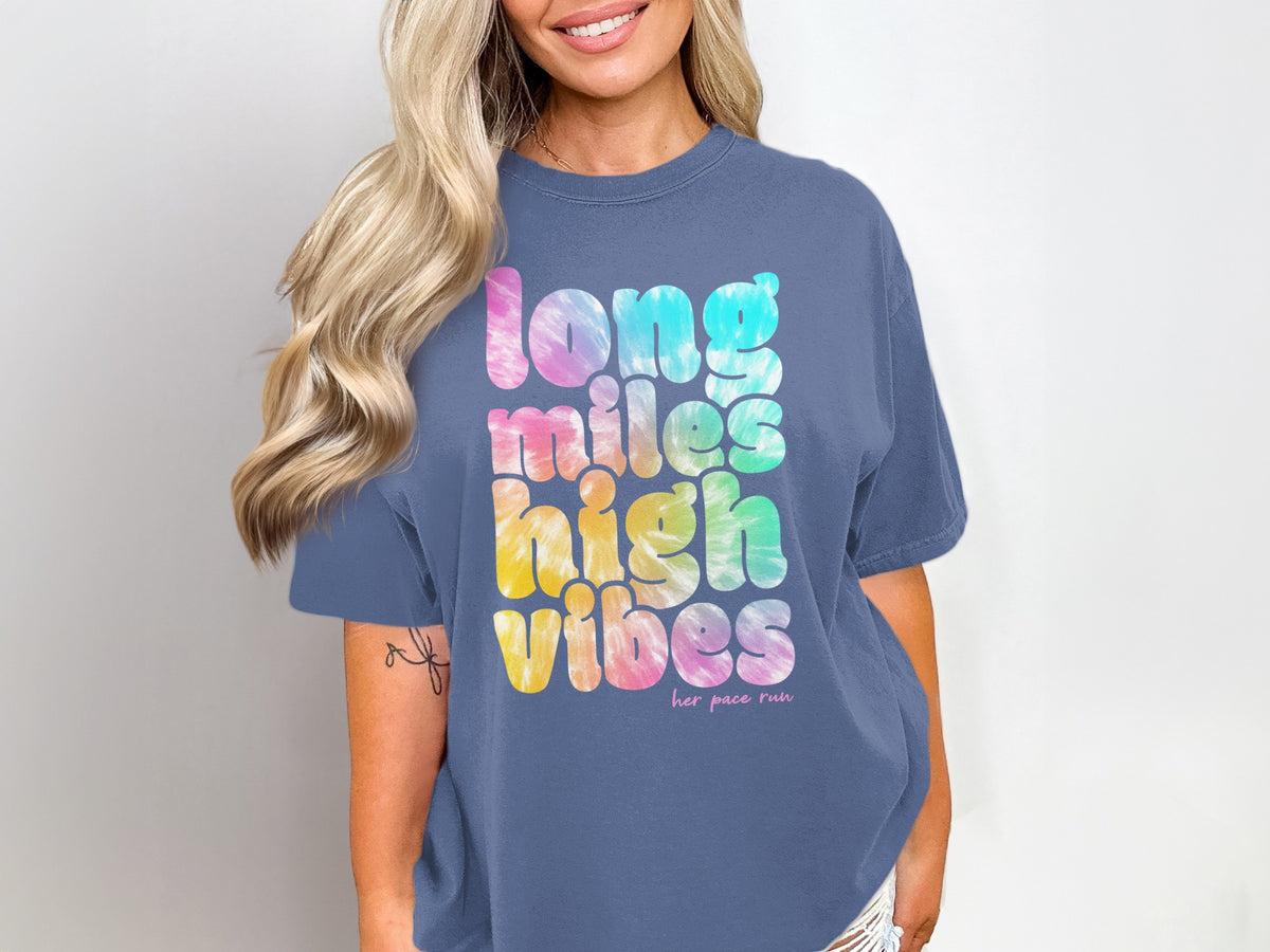 Woman wearing a blue t-shirt with tie-dye text: "long miles high vibes her pace run"