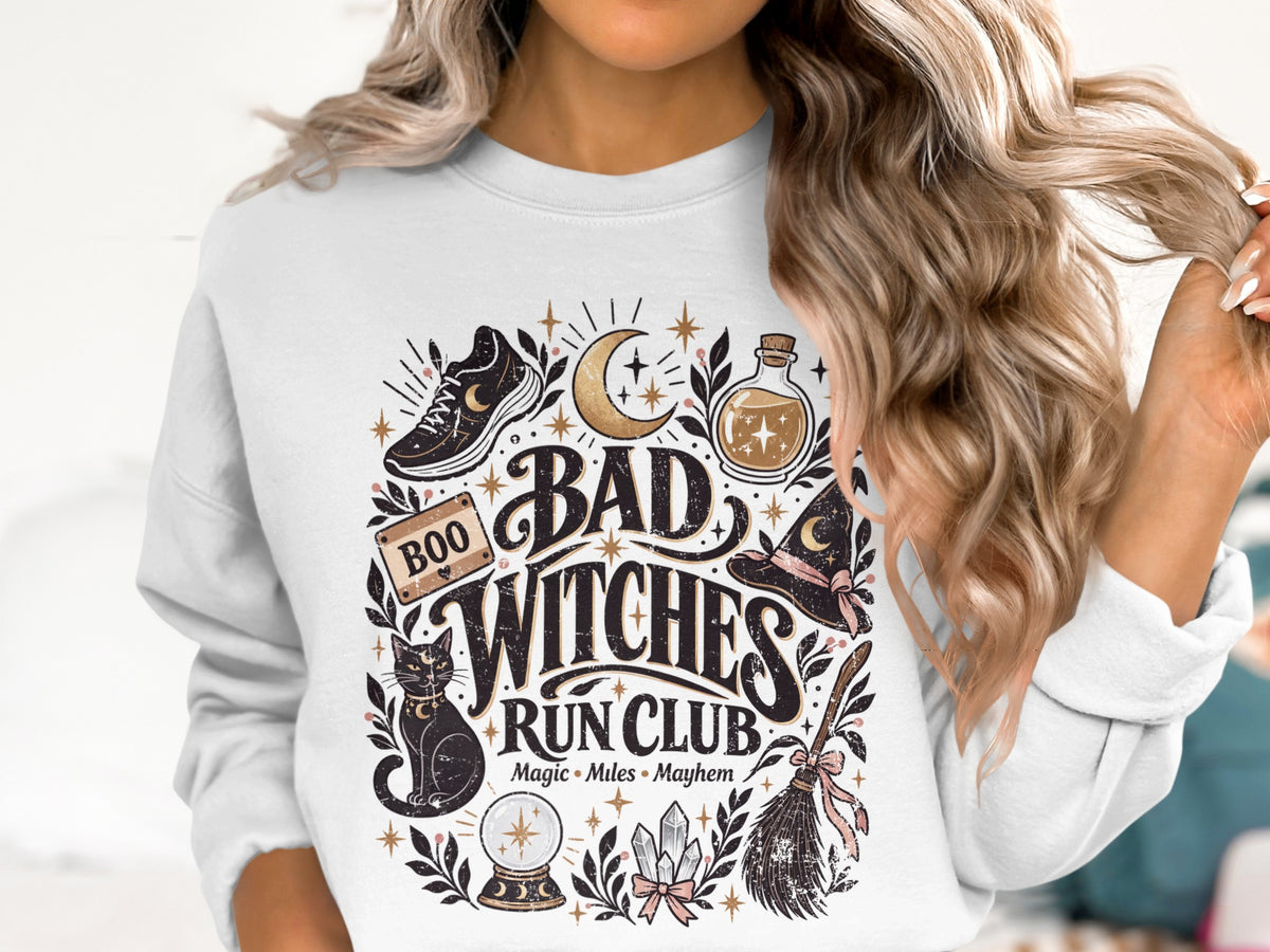 White sweatshirt with "Bad Witches Run Club" graphic featuring a shoe, potion, cat, and broom.