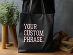 Black tote bag with pink text reading "YOUR CUSTOM PHRASE."