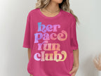 Pink t-shirt with colorful "her pace run club" text in retro font.