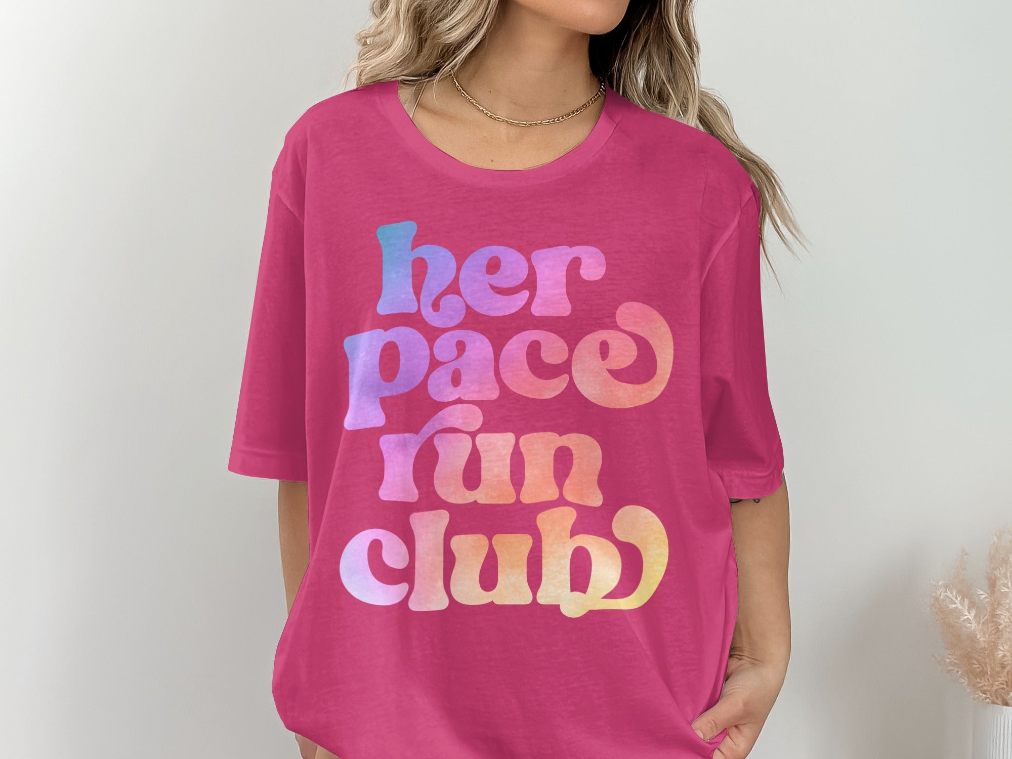 Pink t-shirt with colorful "her pace run club" text in retro font.