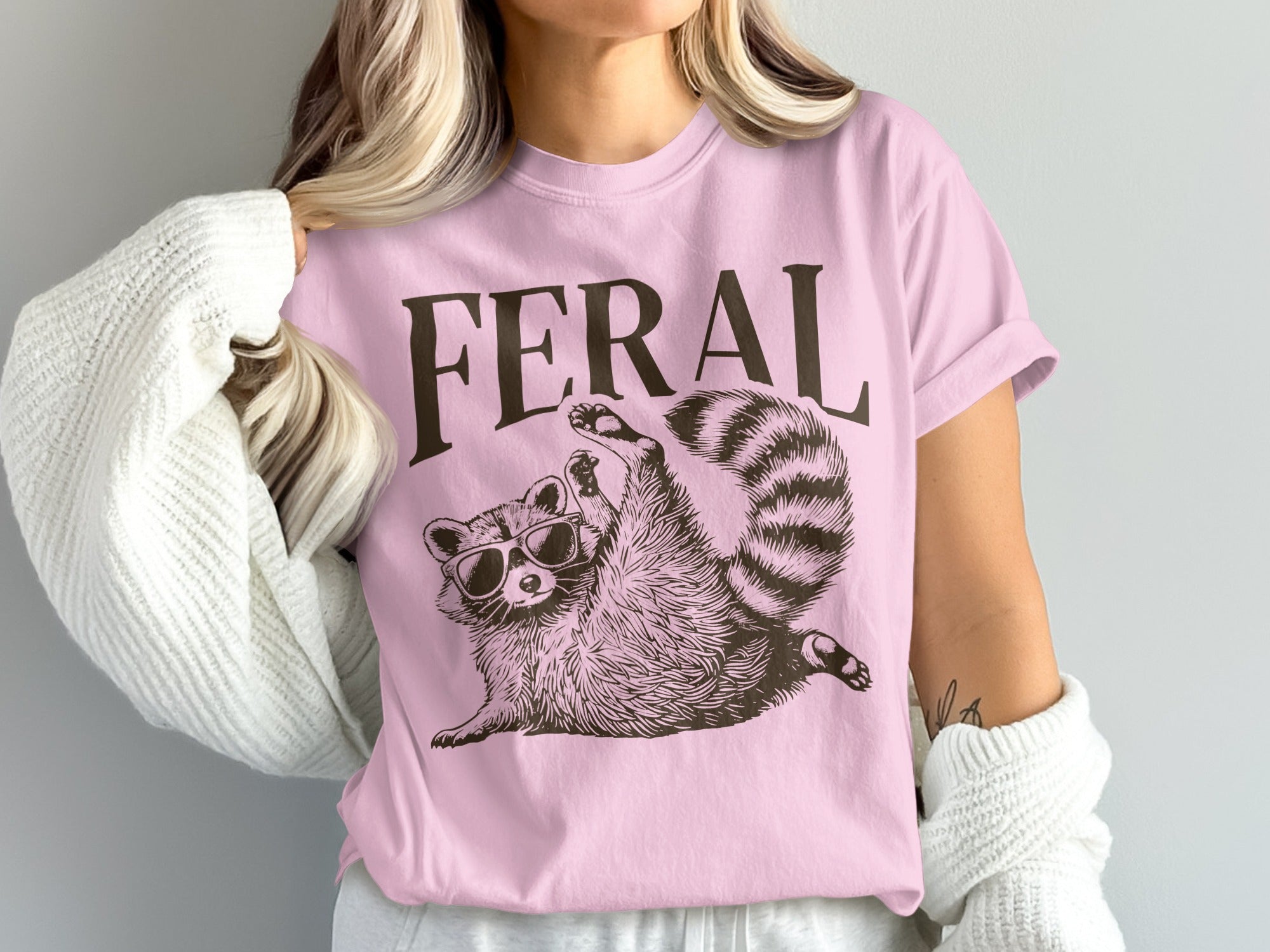 Pink t-shirt with "FERAL" text and a raccoon wearing sunglasses.