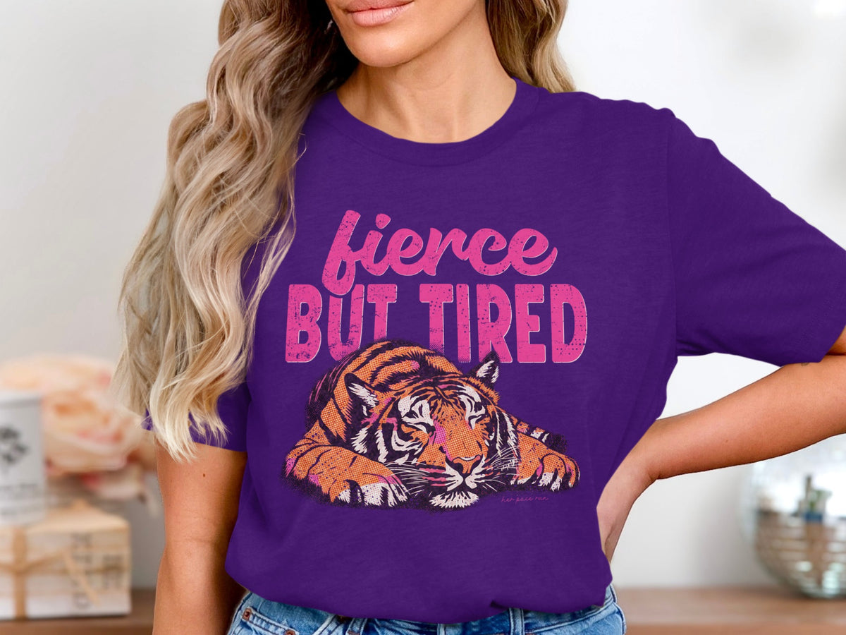 Purple t-shirt with distressed text "fierce BUT TIRED" above a tired tiger graphic.