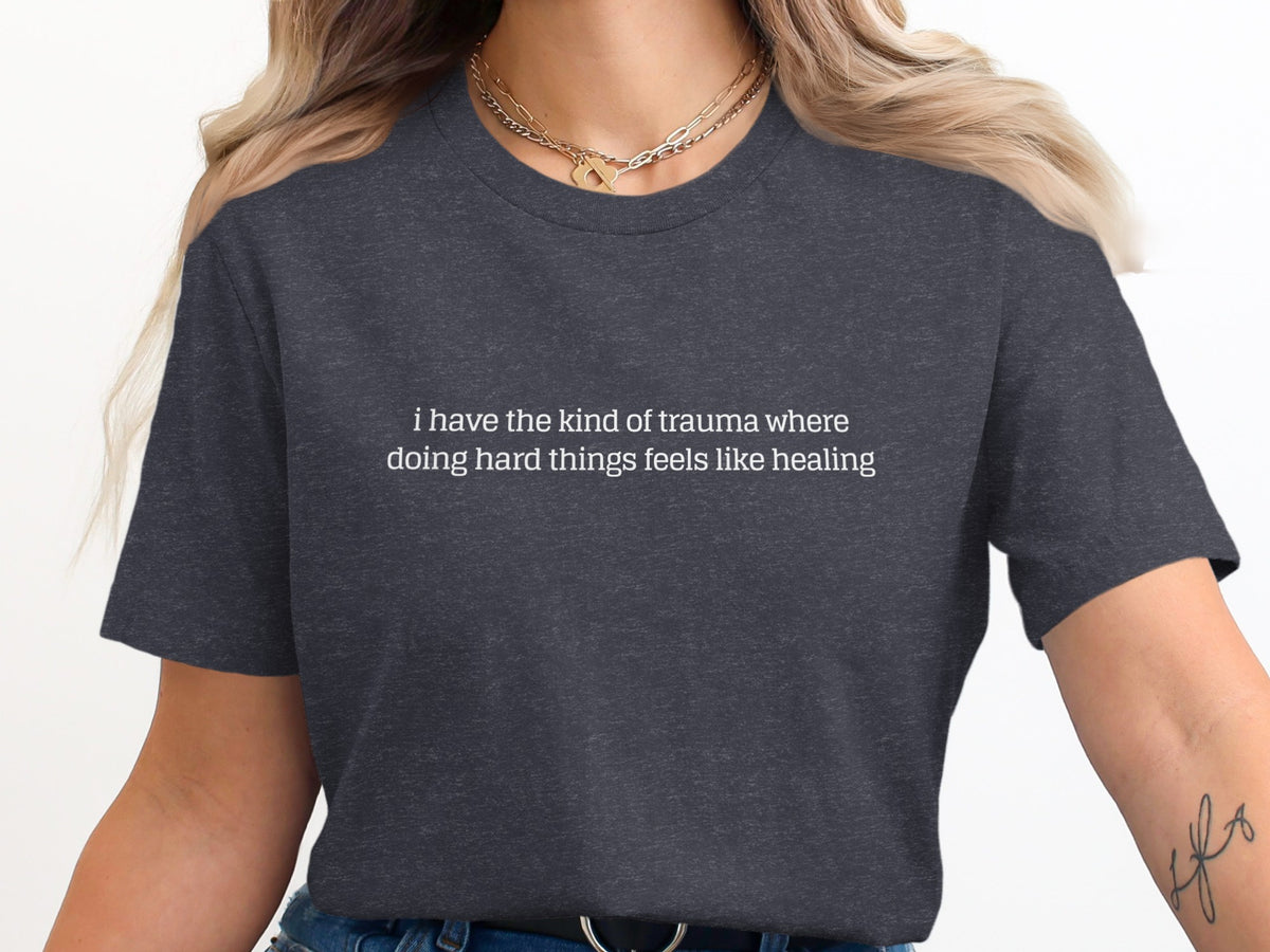 Dark grey t-shirt with white text: "i have the kind of trauma where doing hard things feels like healing"