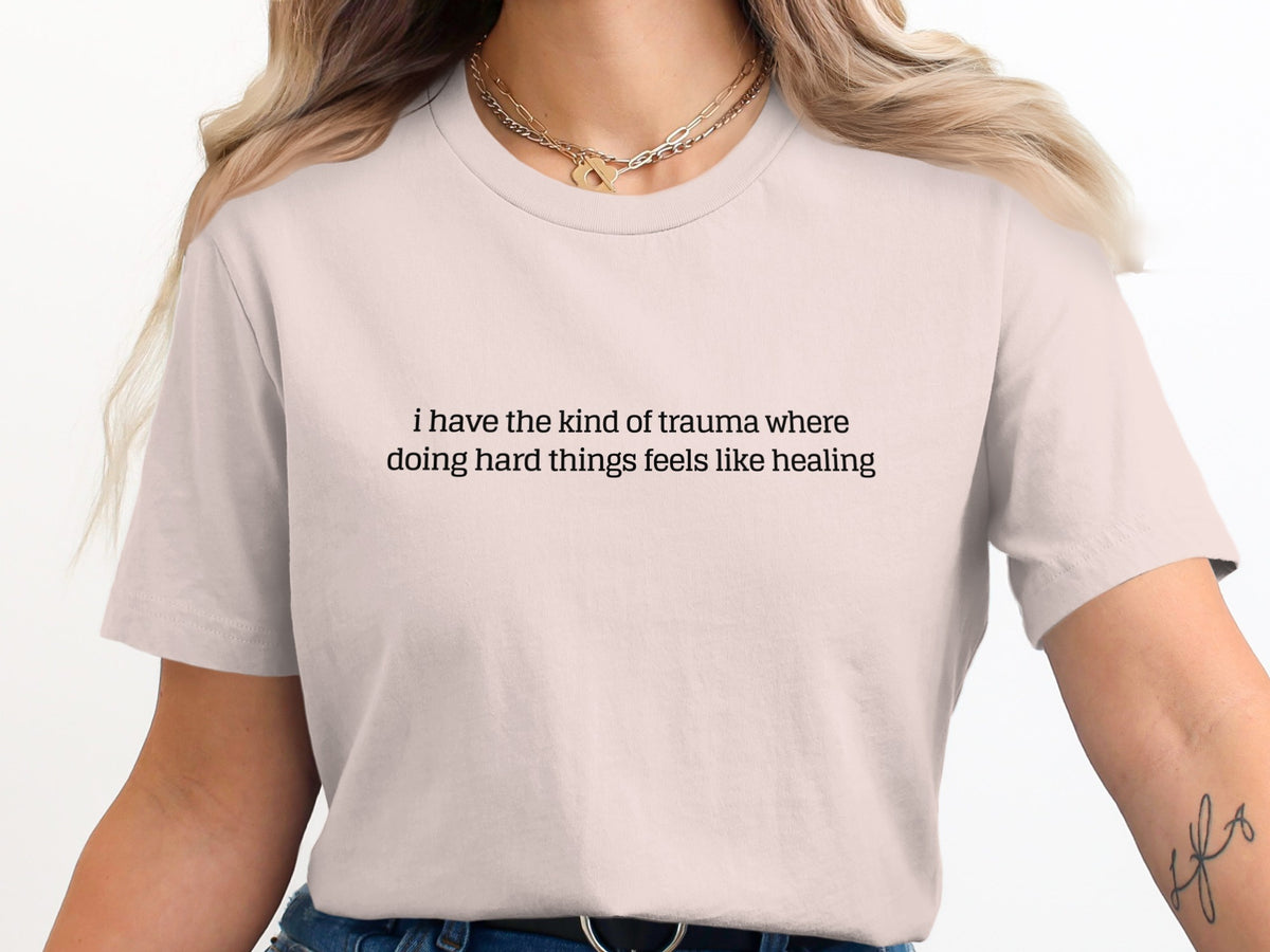 Light pink t-shirt with text "i have the kind of trauma where doing hard things feels like healing".