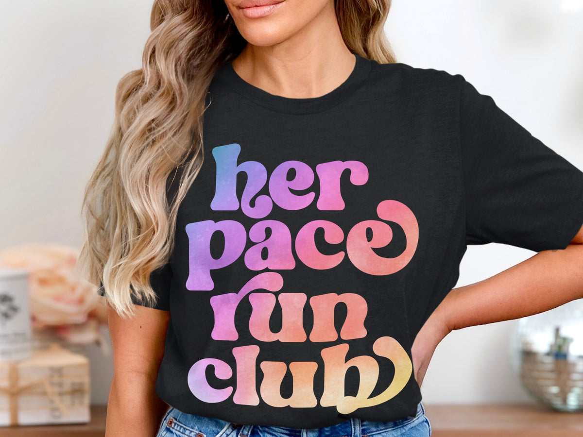 Black t-shirt with "her pace run club" text in pastel gradient letters.