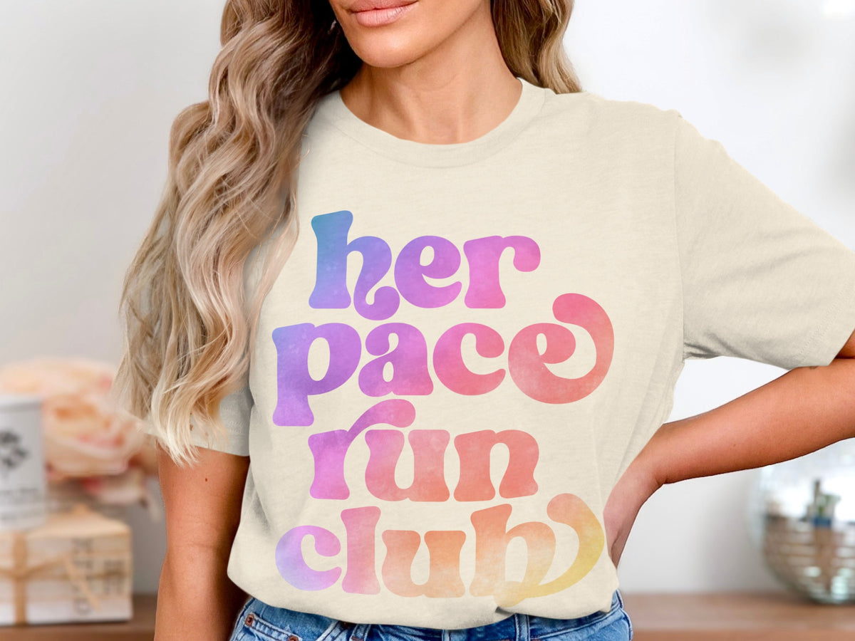 Cream t-shirt with "her pace run club" in gradient watercolor text.