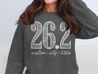 Dark grey sweatshirt with white floral print "26.2 custom city * 2026" design.