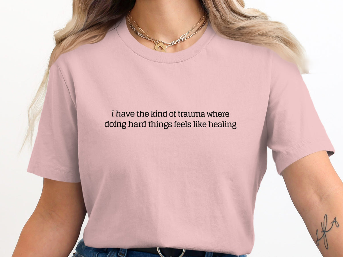 Pink t-shirt with text "i have the kind of trauma where doing hard things feels like healing"