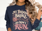 Dark navy sweatshirt with "My broom broke so now I run" text and Halloween graphics.
