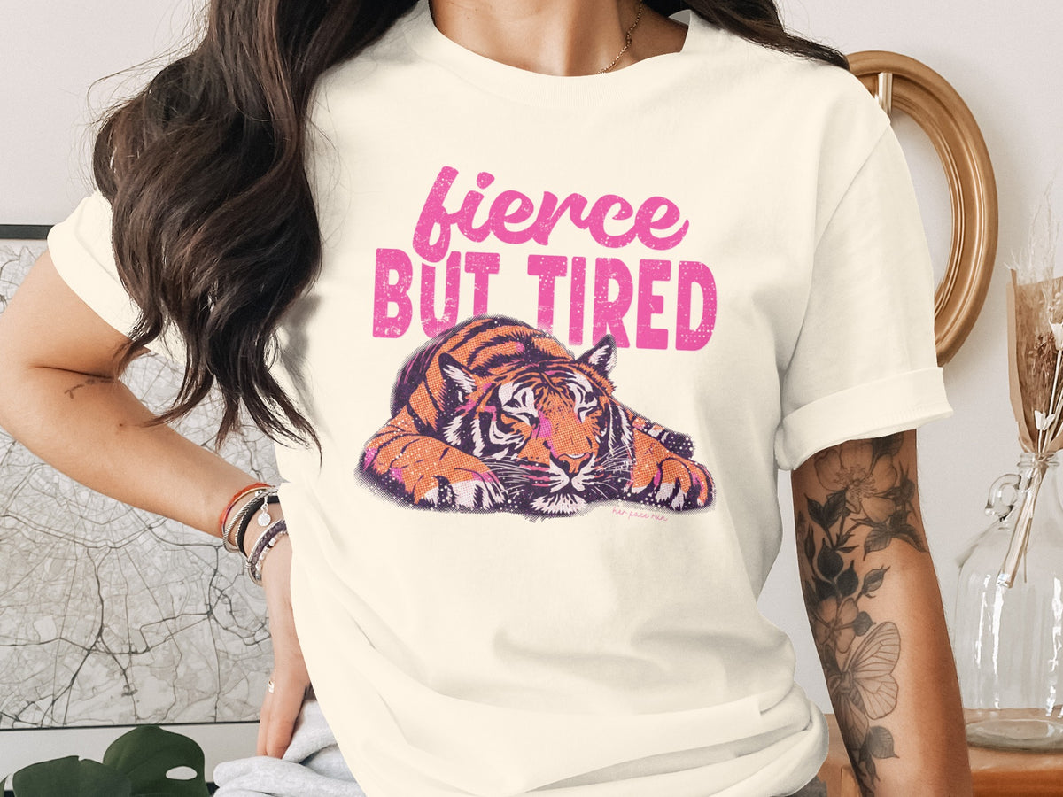 Cream t-shirt with a graphic of a tiger and pink text reading "fierce BUT TIRED".