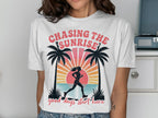 White t-shirt with "Chasing The Sunrise" text and a runner silhouette with palm trees.