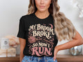 Black t-shirt with "My Broom Broke So Now I Run" text and witch broom design.