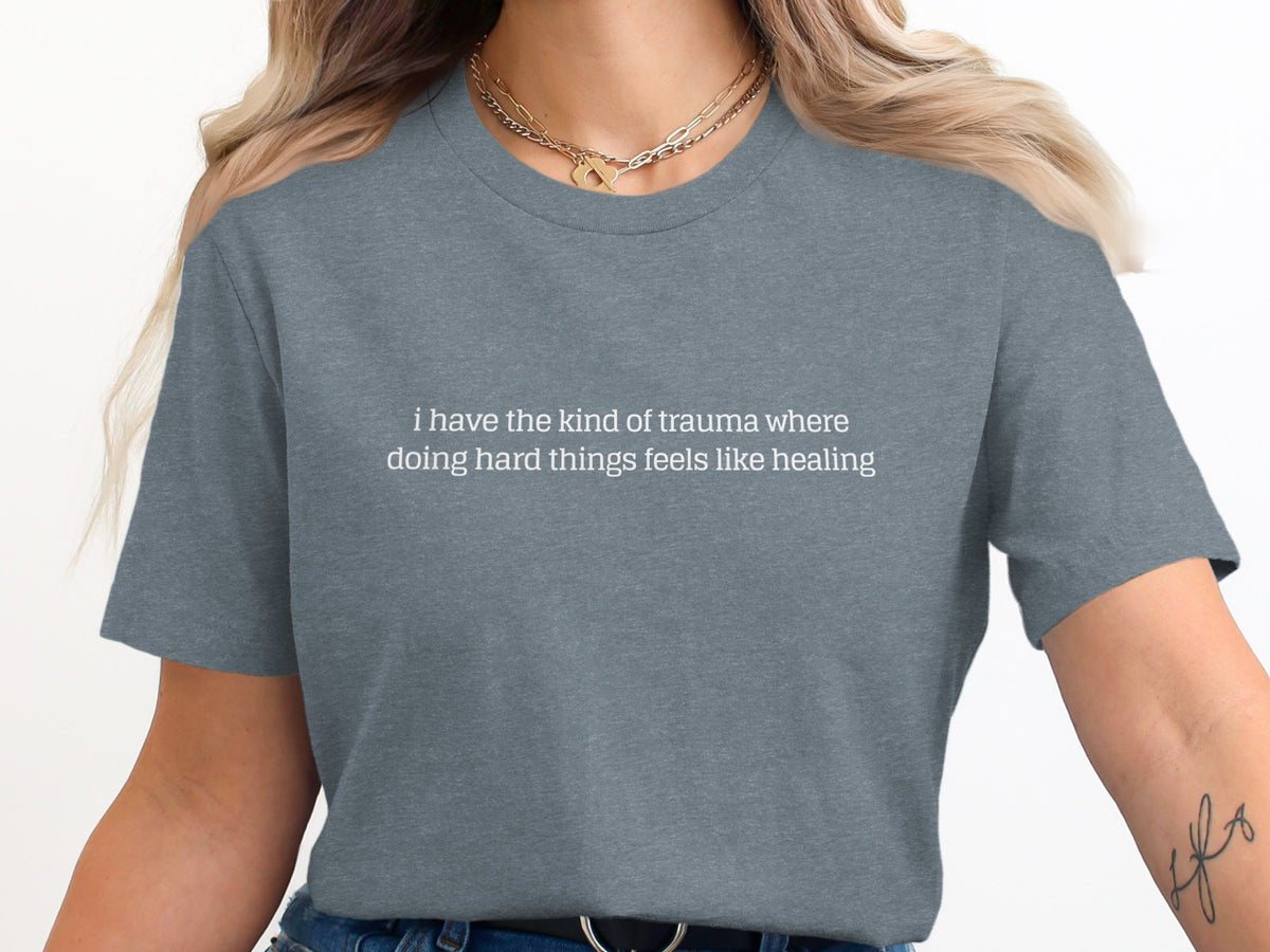 Grey t-shirt with white text: "i have the kind of trauma where doing hard things feels like healing".